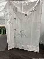 Single curtain panel hung to show full pattern: white fabric with outlined large flowers and leaves in black and beige