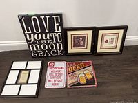 Photo showing all five wall art pieces arranged on the floor against a wall: large text canvas, two framed prints, two metal signs.