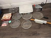 Photo showing assorted bakeware laid out including decorative cupcake stand, marble rolling pin, pie plates, sieve, measuring cup, small containers and bag of cupcake picks.