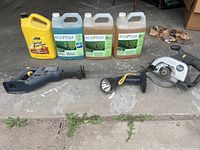Photo showing various garage items including brake fluid container, Eco Max cleaners, reciprocating saw body, flashlight, and Makita circular saw on concrete garage floor.