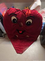 Large red heart-shaped costume displayed flat against a wall, showing facial features and the pointy bottom section.