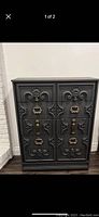 Front view photo of vintage dresser showing black and gold refinish with ornate carved drawer fronts and brass handles.