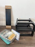 Two sets of black furniture legs and a container with assorted hardware including cabinet brackets and repair parts.