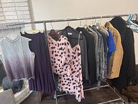 Full view of assorted business casual clothes on rack, showing variety of tops, dresses, jackets, and coats mostly in dark and neutral colors with some bright accents.