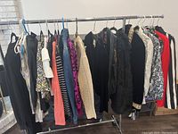Full view of the assorted ladies clothes on a rack showing a variety of tops, sweaters, jackets including knit, denim, and fur-like materials and patterns.