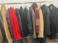 Row of ladies coats, jackets, and blazers on rack showing front and sides with variety of colors and styles