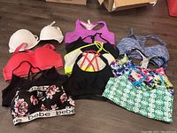 Photo of assorted ladies sports bras in various colors, patterns, and strap styles on a wooden floor.