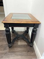 Solid wood square end table with black painted legs and natural wood top with glass insert, showing side view.