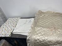 Photo showing folded floral flat sheet, white flat sheet, pillow shams and satin decorative sham placed on a shelf