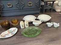 Photo showing full assortment laid on floor including amber glass bowls, colorful ceramic dish, white covered dishes, green glass dish, salt and pepper shakers, gravy boat, and ceramic bird figurines.