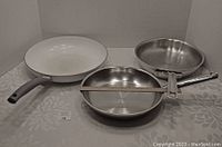 Three fry pans viewed from above showing one ceramic-coated pan and two stainless steel pans with measuring stick indicating 10 inch diameter.