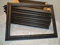 Ten identical carved wood picture frames stacked and displayed on a surface, showing decorative carved patterns and dark finish.