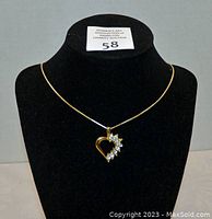 Front view of the necklace displayed on a black velvet bust showing the gold-tone heart pendant with clear crystals arranged elegantly on one side.
