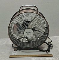 Front view of General Supply electric fan showing shiny metal grille and brand logo at center.