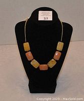 Front view showing the necklace on a display bust, highlighting the rectangular butterscotch and cream cut stone beads arranged alternately on a gold-tone chain.