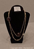 Full length view of gold tone double-layer necklace with two dark spherical pendants displayed on black velvet neck stand.