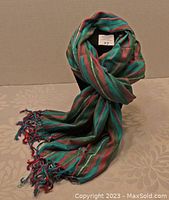 Photo showing the scarf loosely draped with visible turquoise, rose, and pink horizontal stripes, displaying texture and fringed ends.