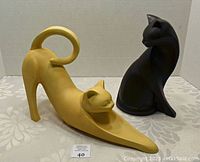 Yellow cat figurine stretching with forward legs and curved tail, black cat figurine sitting grooming face behind it