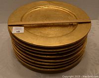 Stack of eight gold ceramic charger plates with a wooden ruler showing approximately 12 inches diameter.