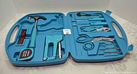 Open blue carrying case showing hand tools inside molded compartments including hammer, staple gun, measuring tape, pliers, scissors, and screwdrivers