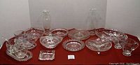 Full lot view showing all clear glass dishes and serving pieces with cornflower pattern on red cloth background