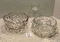 Two clear cut crystal bowls and one long-stemmed crystal glass displayed on patterned surface, showing overall set condition.