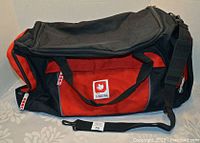 Closed view of the Molson Canadian hockey bag showing logo on red front panel, black accents, handles with Velcro, and shoulder strap.