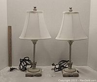 Front view of two matching table lamps with white fabric shades, decorative textured bases, and owl finials. Electrical cords placed in front.