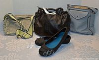 Front view of three purses standing upright and pair of black flat shoes laid in front, showing all items and their condition.