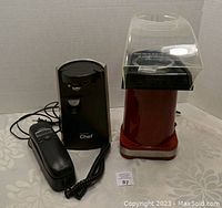 Full view of the three items showing the Cuisinart popcorn popper, Master Chef can opener, and corded phone placed on a patterned tablecloth.