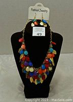 Front view of multi-layer necklace with colorful beads and gold leaf charms displayed on black stand with matching earrings on a white card.