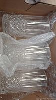 Three crystal highball glasses arranged in a cardboard box with bubble wrap protection, showing diamond and vertical cut patterns.