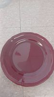 Top view of a single red ceramic plate showing scalloped edges and glossy finish.