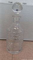 Front view of clear crystal decanter with stopper on a flat surface.