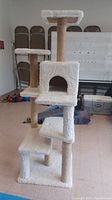 Front view of tall multi-level cat tree with multiple platforms, cubby, and beige sisal-wrapped scratching posts, white plush covering