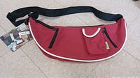 Side angle of the KOIE red shoulder bag with tags visible, showing zipper pockets and white trim.