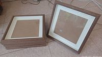 Four wooden picture frames shown stacked and one standing to display the front view with white mat and medium brown wood border.