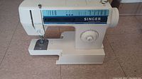 Overall front and side view of the white Singer sewing machine showing sewing area, needle, and stitch selection panel.