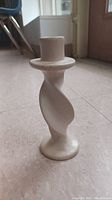 Single off-white ceramic candle holder with twisted design on floor