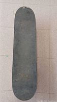 Top side of skateboard deck showing worn black grip tape with scuffs.