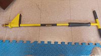 Full length view of the yellow metal stand up weeder showing the claw head digging tool and handle.