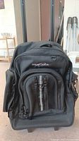 Front view of the black Tracker rolling backpack showing multiple zippered compartments and brand name embroidered on the top compartment.