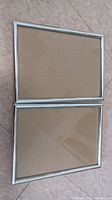 Two silver rectangular picture frames stacked on floor, showing full view of both frames.