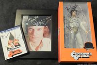 Three items grouped together on black surface: DVD, framed photo, action figure