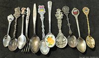 Photo of 10 collector spoons and one fork, showing a variety of detailed handles and bowl designs including colored enamel and sculpted figures
