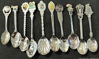 Photo showing eleven collector spoons in a row, with various decorative handles and emblems representing places and themes.