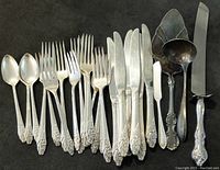 Full layout of silverware showing 3 teaspoons, 7 forks, 7 knives, 1 pie server, 1 ladle, and 1 cake knife placed on a dark surface.