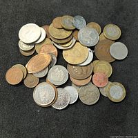 Mixed pile of world coins and pressed pennies showing multiple designs and materials on black background.