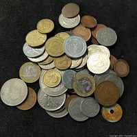 Pile of assorted world coins and tokens in various metals and designs on black background.