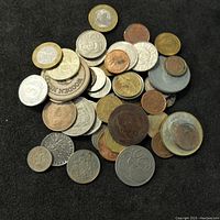 Overview image of assorted world coins and tokens on black background showing a variety of sizes and metal types.